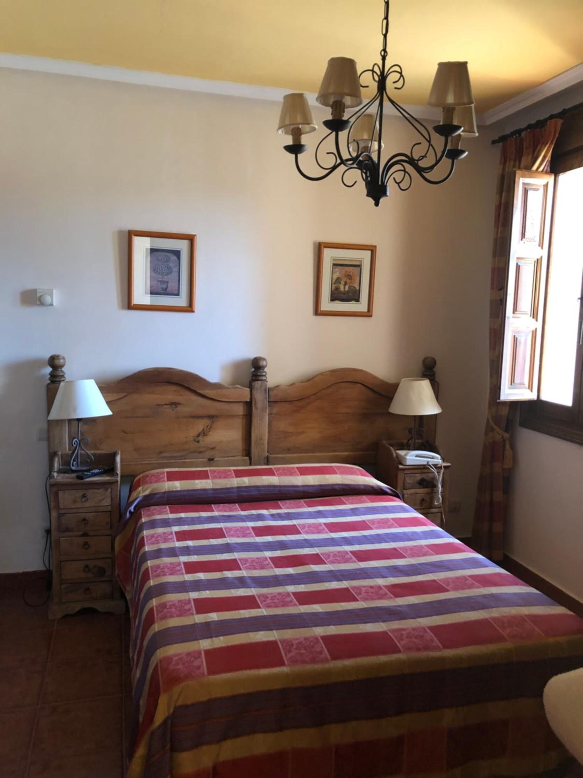 A bedroom with a wooden headboard, a bed with a striped blanket, two bedside tables with lamps, and two framed pictures on the wall.