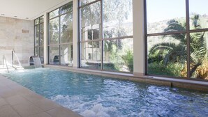An indoor swimming pool with large windows, a water slide, and a view of palm trees.