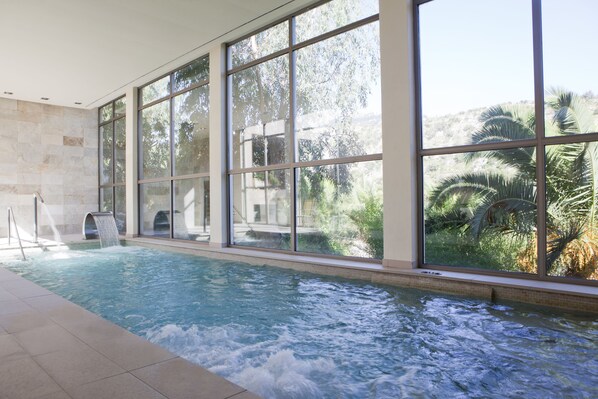 Una piscina interior con amplias ventanas, un tobogán de agua y vistas a palmeras.