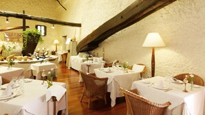 A restaurant with multiple tables set for dining, featuring wicker chairs and white tablecloths.