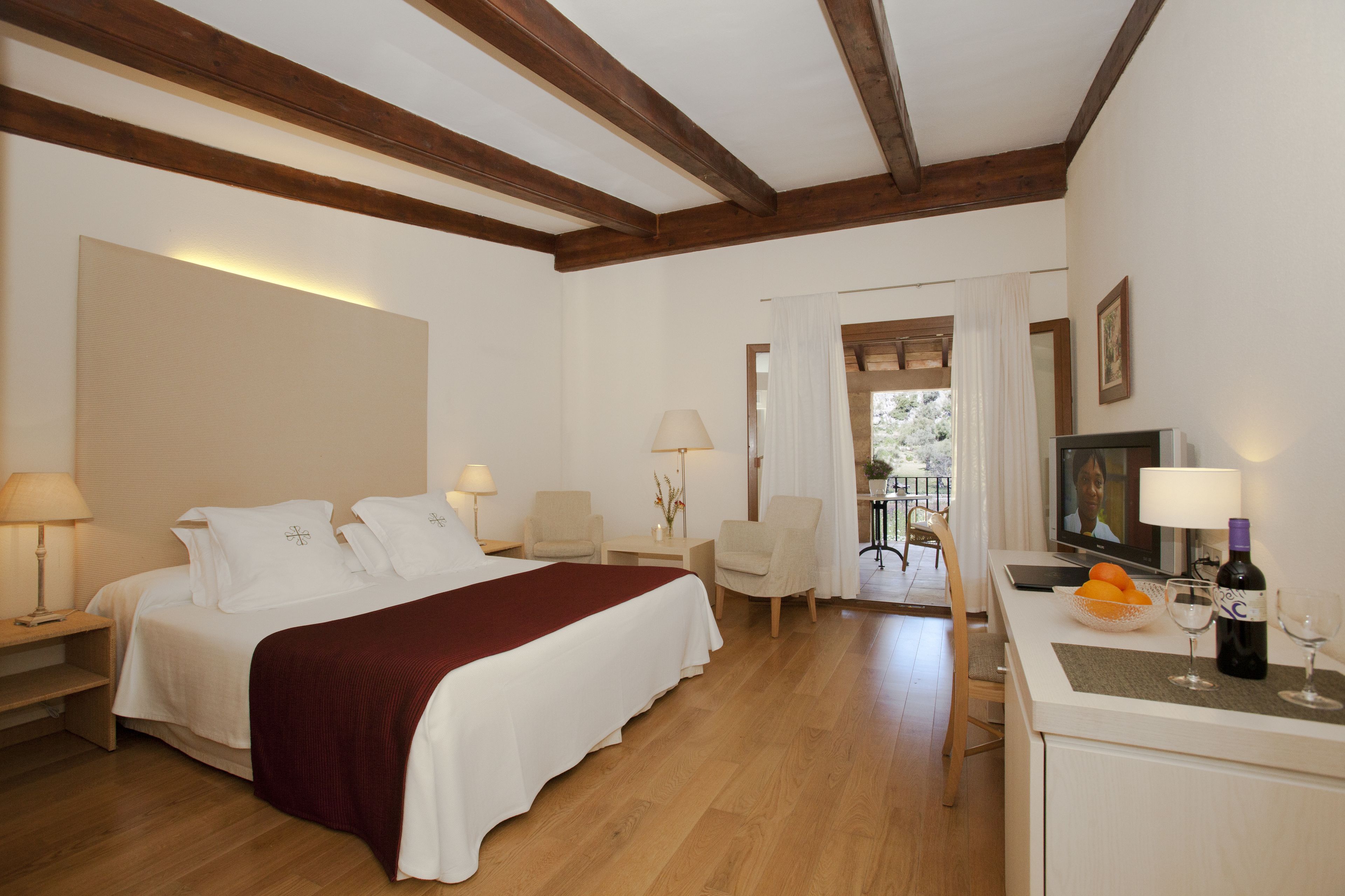 Une chambre d’hôtel avec un grand lit, deux tables de chevet, un bureau, une chaise, une télévision et une bouteille de vin.