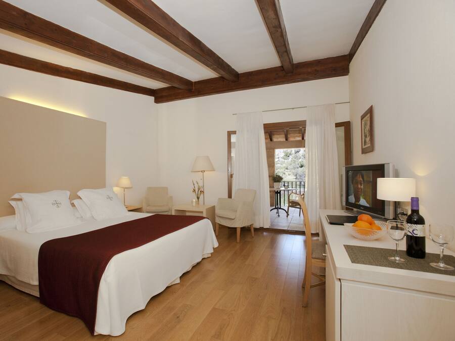 Habitación de hotel con una cama grande, dos mesitas de noche, un escritorio, una silla, un televisor y una botella de vino.