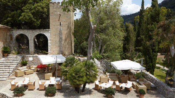 An outdoor patio with stone flooring, multiple seating areas, and potted plants.