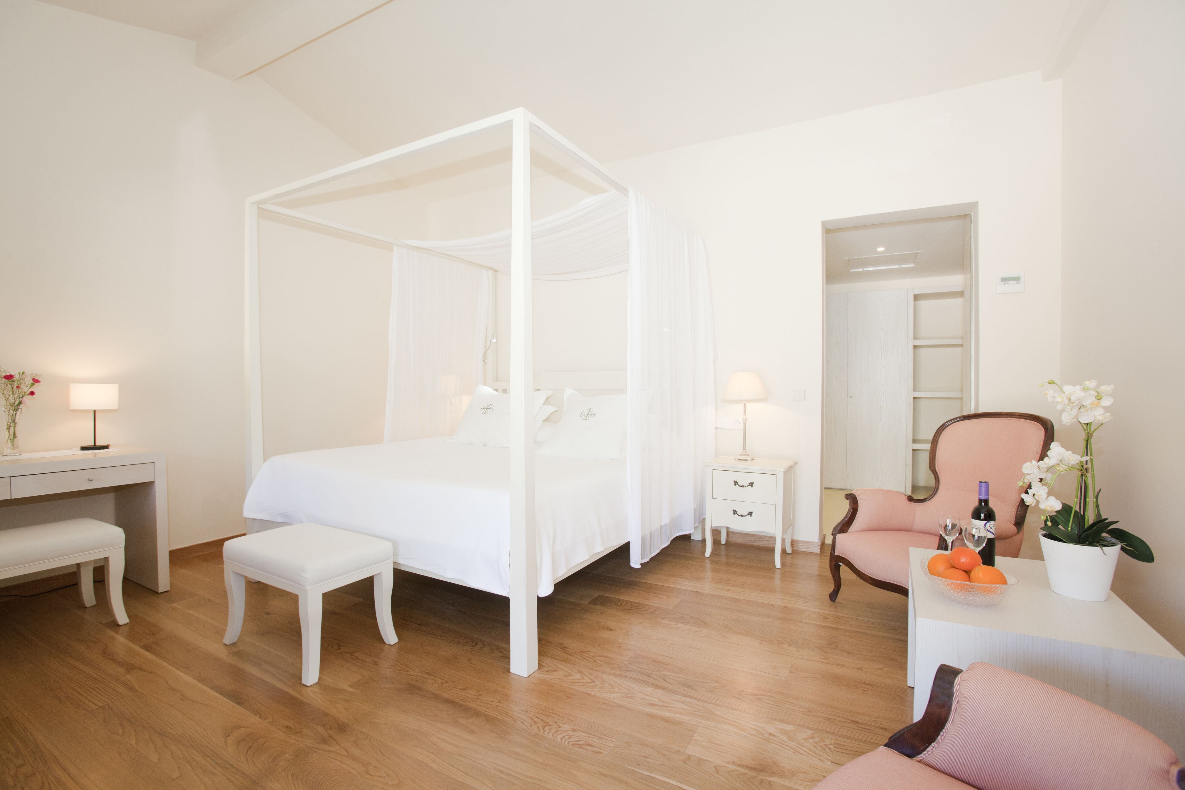 Une chambre à coucher avec un lit à baldaquin, une table de chevet avec une lampe, une chaise, un bureau avec une lampe et une petite table sur laquelle se trouvent une bouteille et des fleurs.