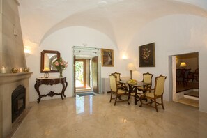 Un comedor con piso de mármol, chimenea, una mesa con sillas y un espejo sobre un mueble aparador.
