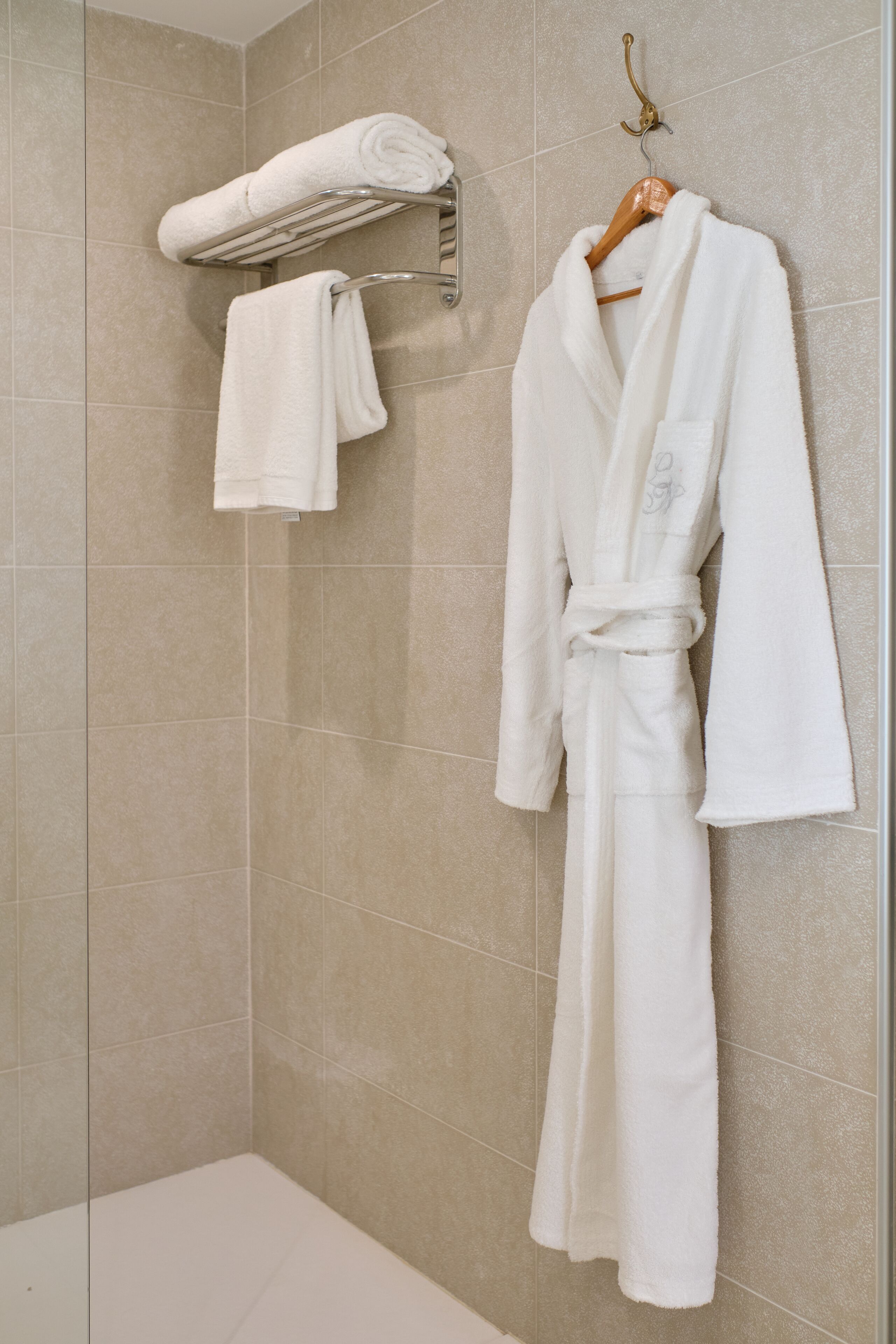 A bathroom with a white bathtub, a towel rack with a folded towel, and a white robe hanging on the wall.