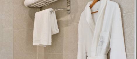 A bathroom with a white bathtub, a towel rack with a folded towel, and a white robe hanging on the wall.
