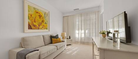 Un soggiorno moderno con un divano color beige, un tavolino, una televisione e un quadro appeso al muro.