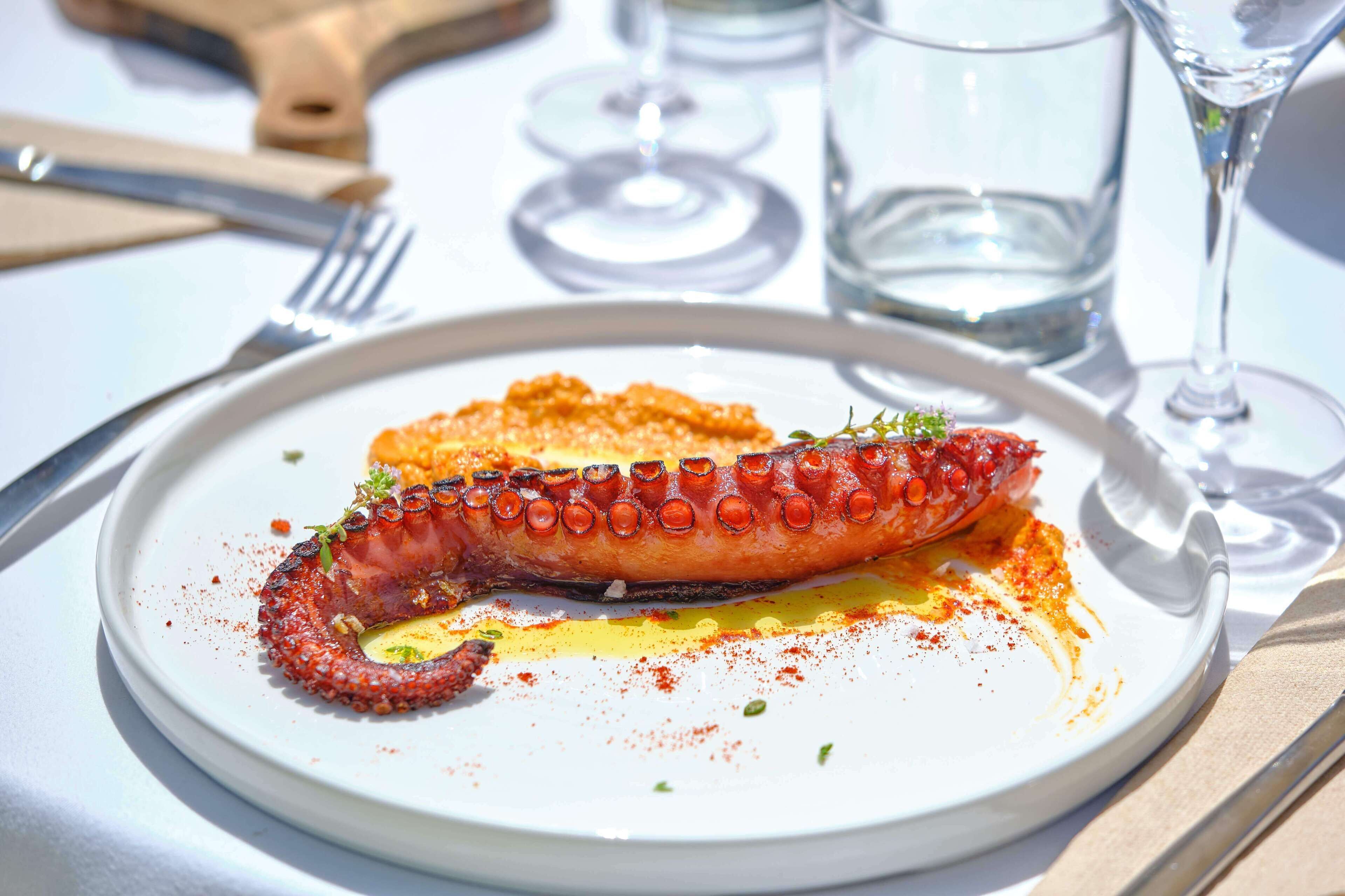 A plate with grilled octopus, a fork, and a knife on a table.