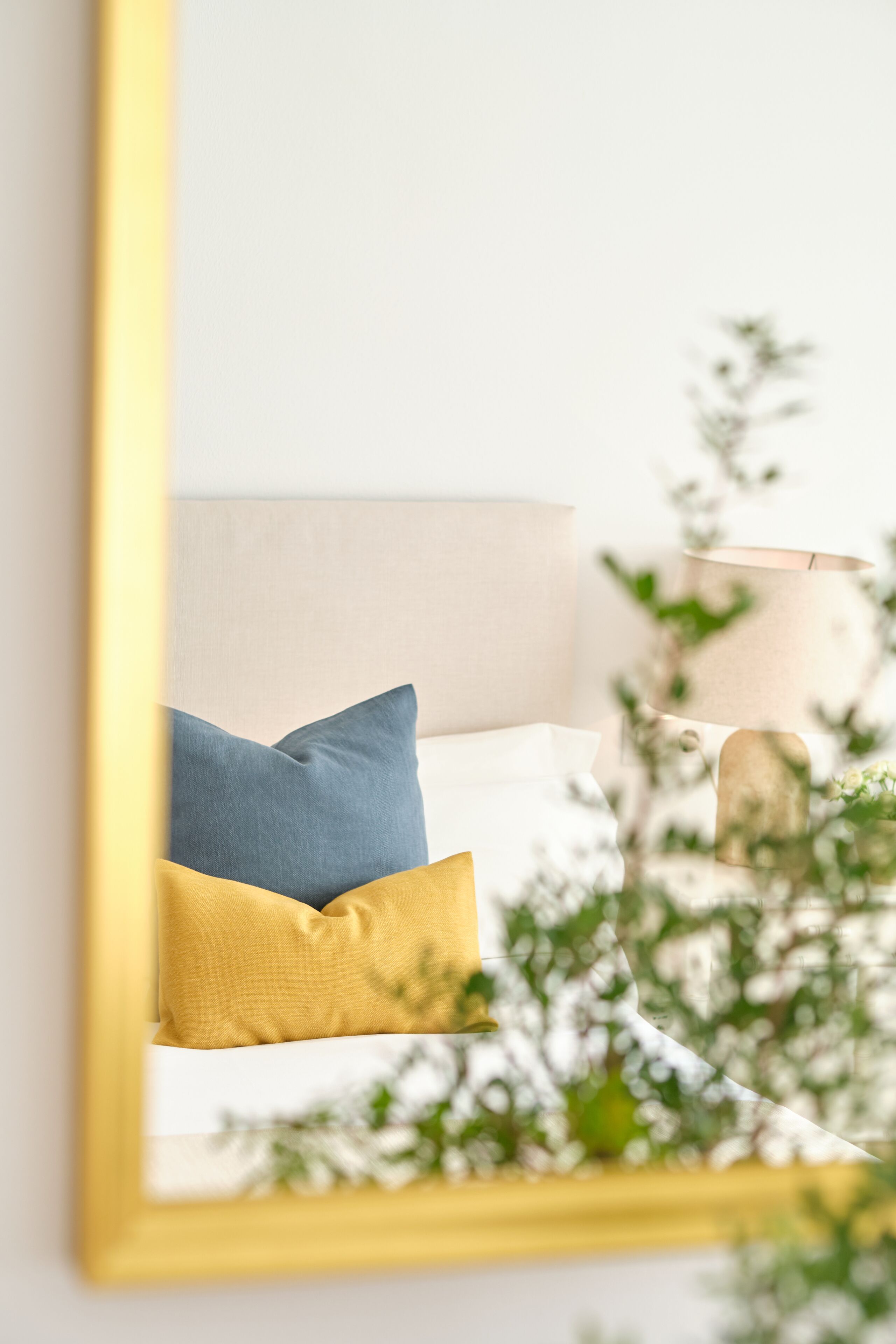 A bed with two pillows, a bedside lamp, and a plant in the background.