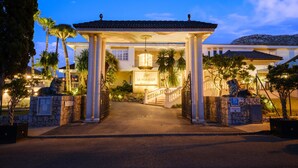 Entrada de un hotel con un vestíbulo cubierto, palmeras y una montaña al fondo.
