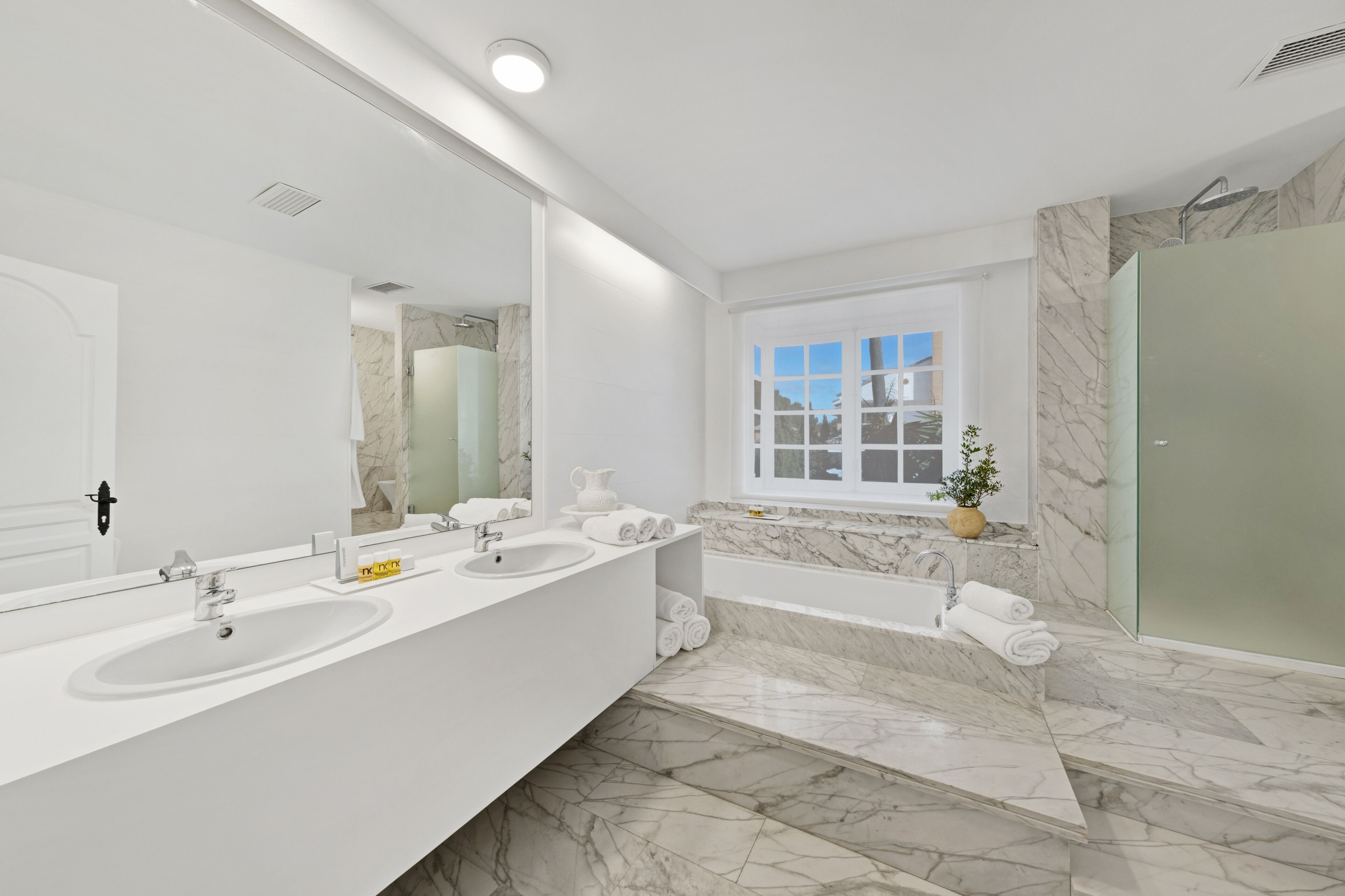 Un baño moderno con dos lavamanos, un espejo grande, una bañera y una ventana con vistas.