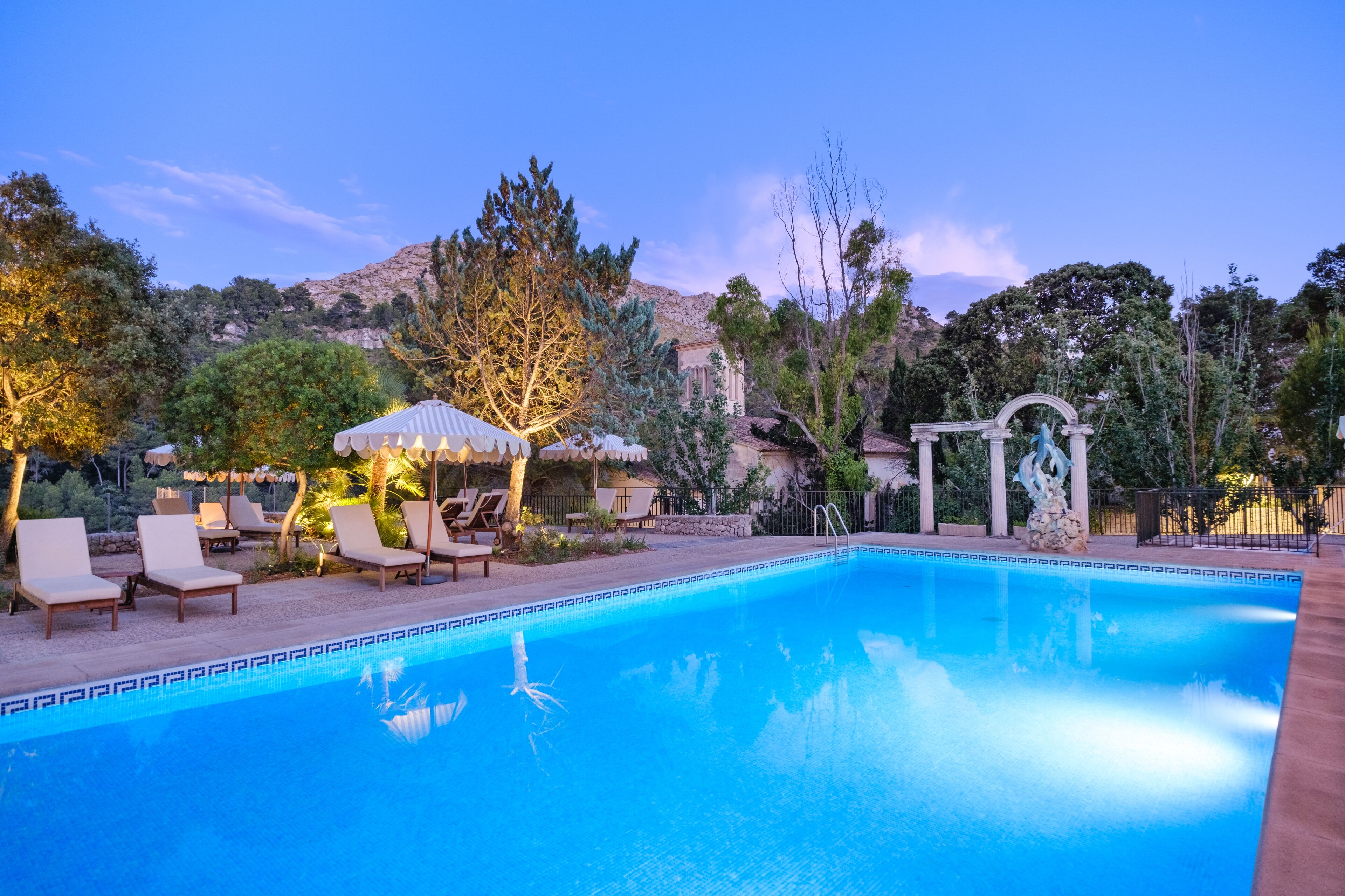 A swimming pool with lounge chairs and a gazebo, surrounded by trees and a mountainous backdrop.
