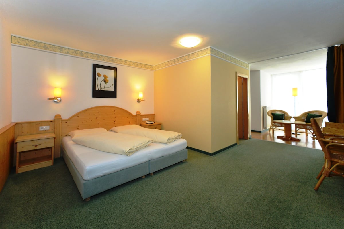 A hotel room with a bed, bedside tables, a desk, and chairs.