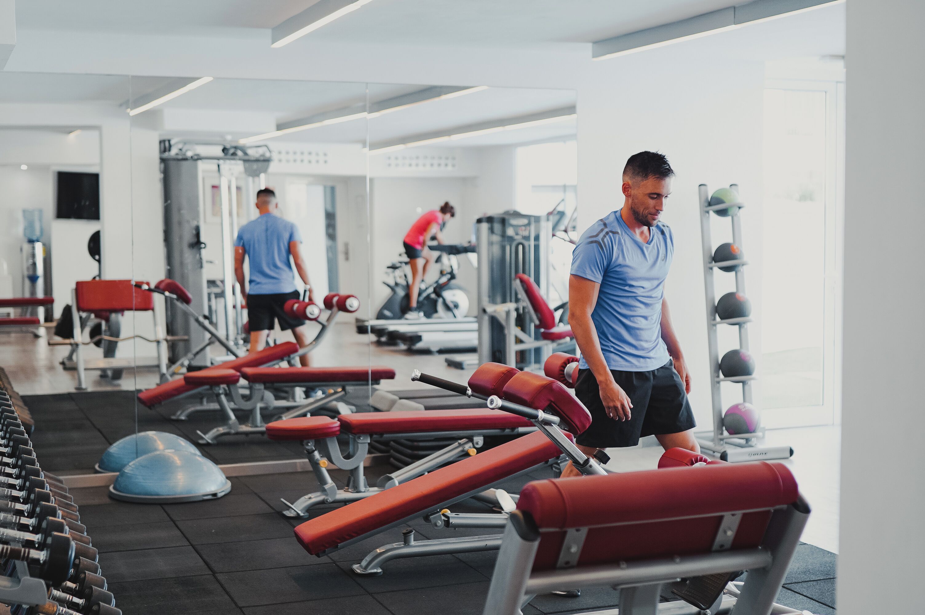 Gimnasio con equipo de ejercicio, una persona caminando y otra entrenando.