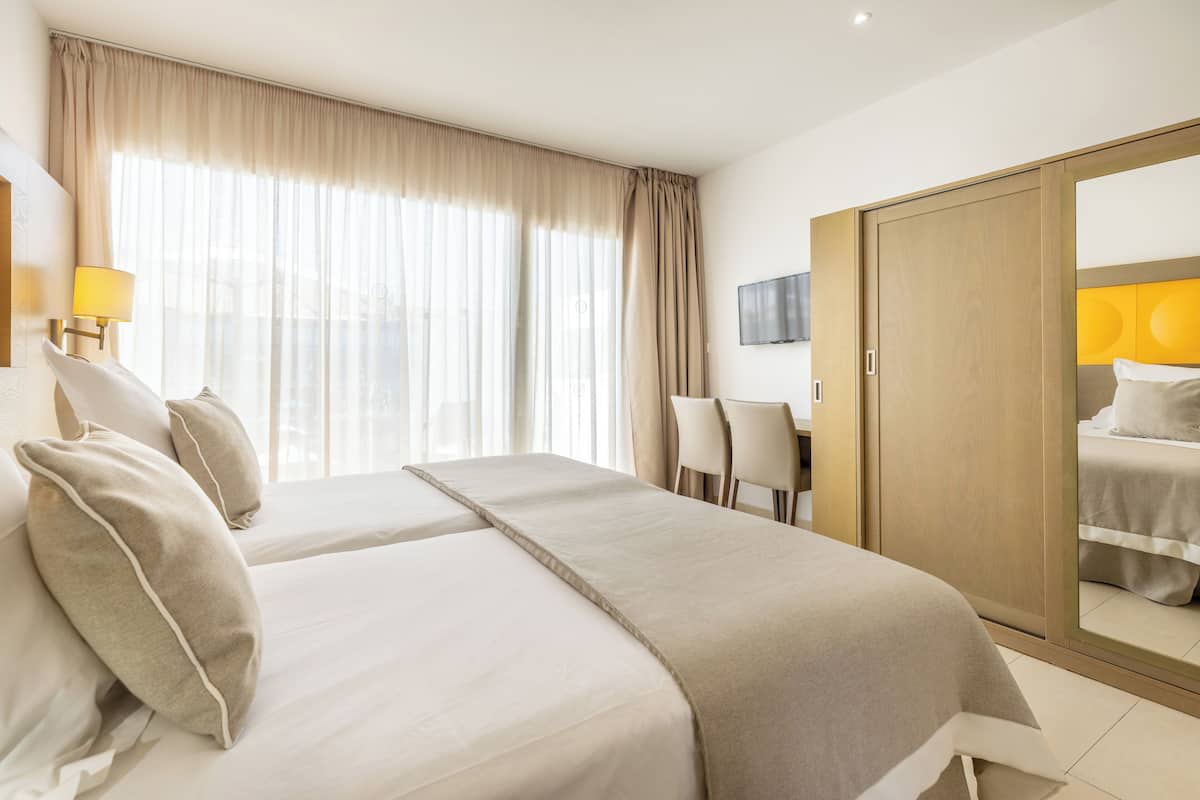 A hotel room with a large bed, a desk, and a wardrobe.