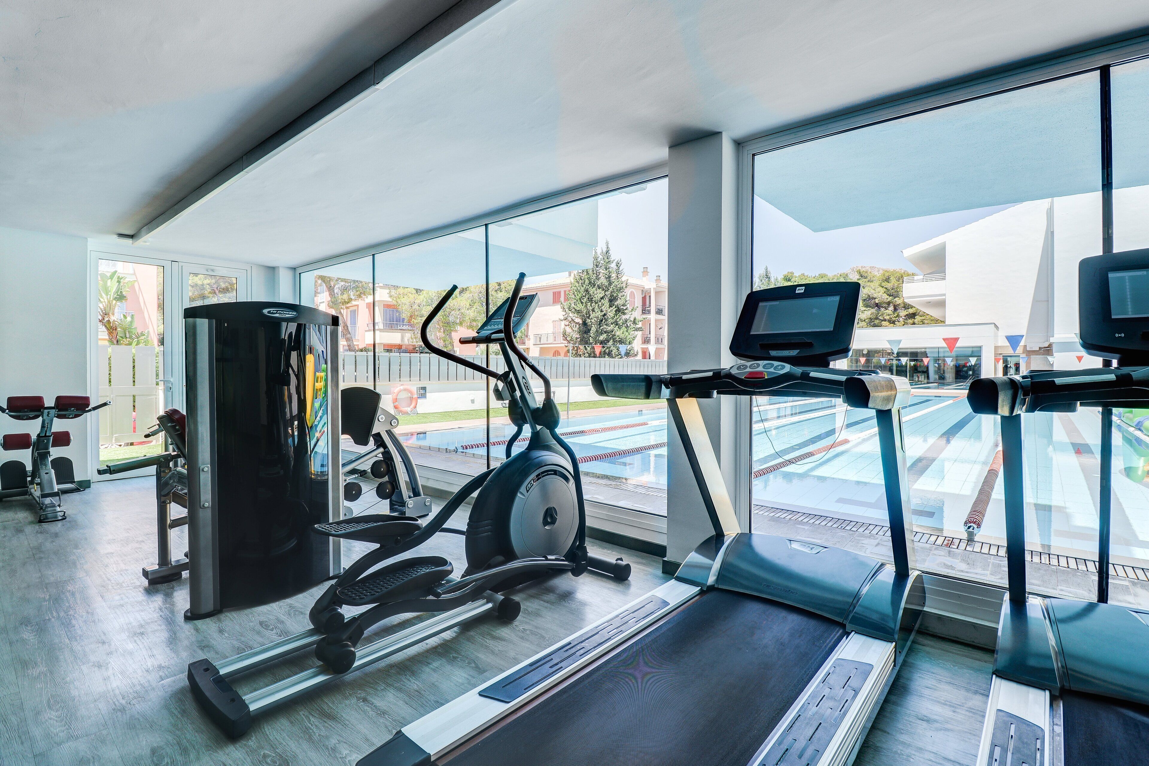 A modern gym with cardio equipment, weight machines, and a large window offering a view of the outside.