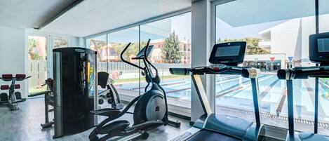A modern gym with cardio equipment, weight machines, and a large window offering a view of the outside.