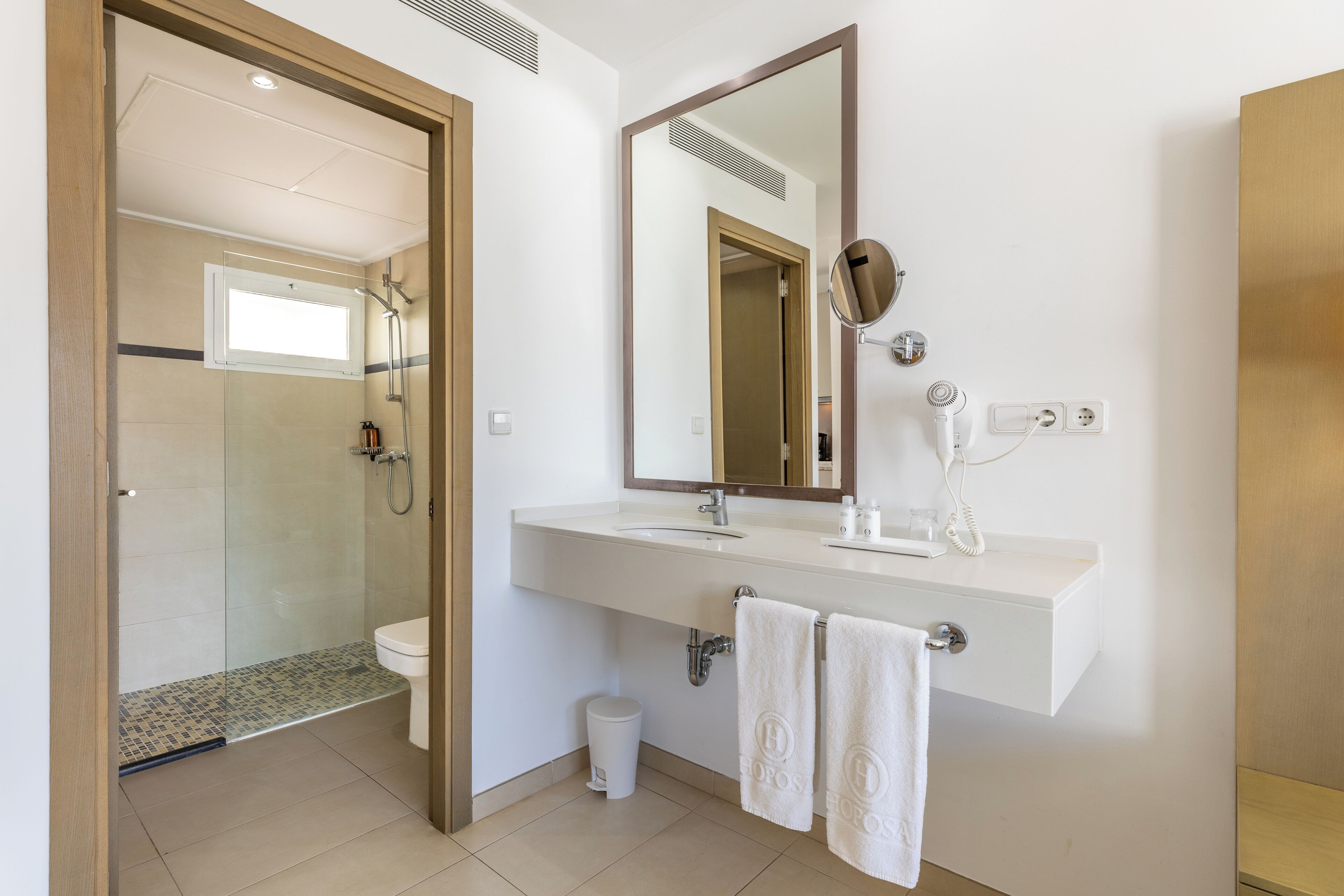 Un baño moderno con cabina de ducha de vidrio, un lavabo blanco con espejo y dos toallas colgadas en ganchos.