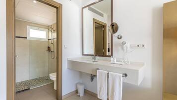 Un baño moderno con cabina de ducha de vidrio, un lavabo blanco con espejo y dos toallas colgadas en ganchos.