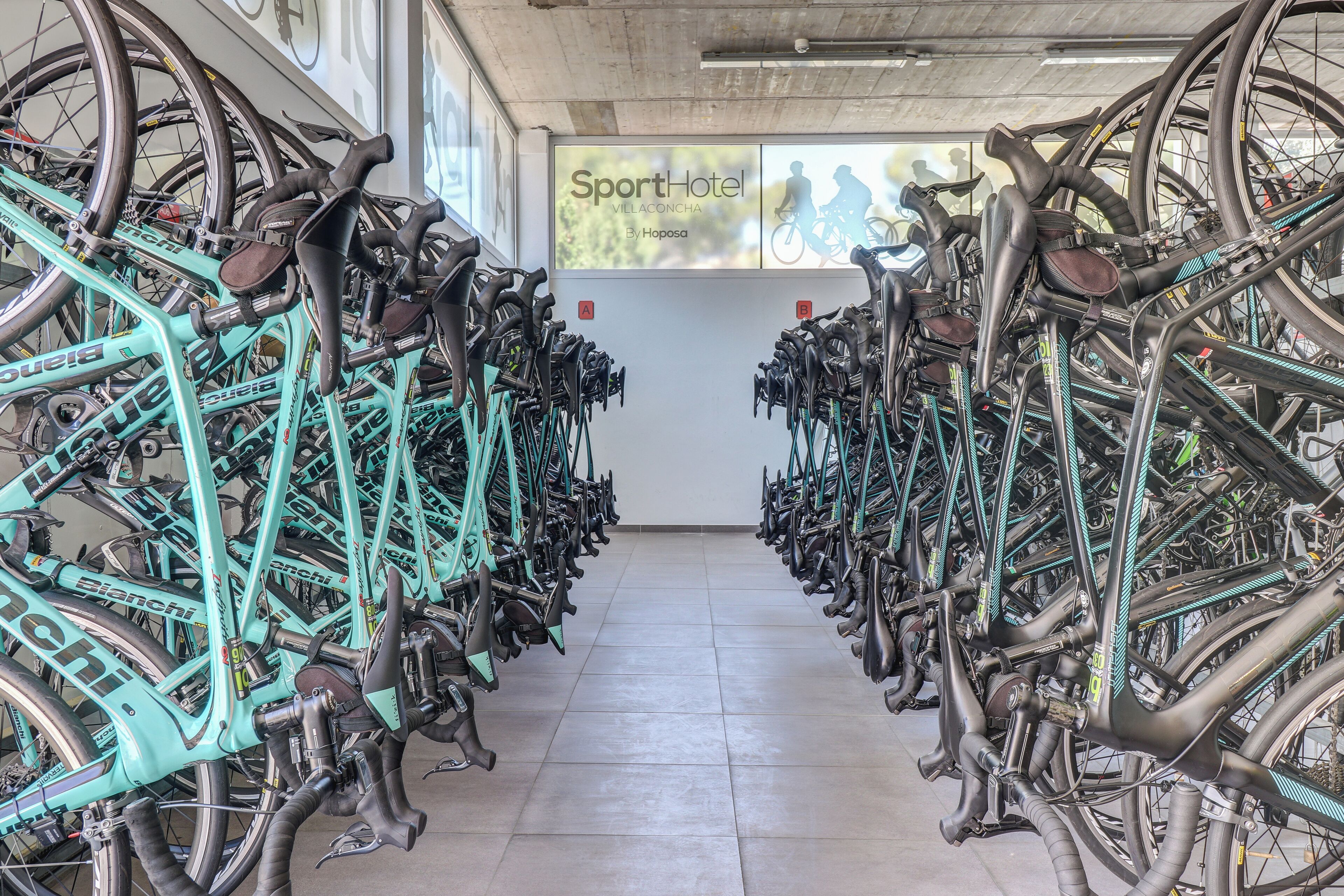 A bike rental station with numerous bicycles, a sign for SportHotel Villaconcha, and a tiled floor.