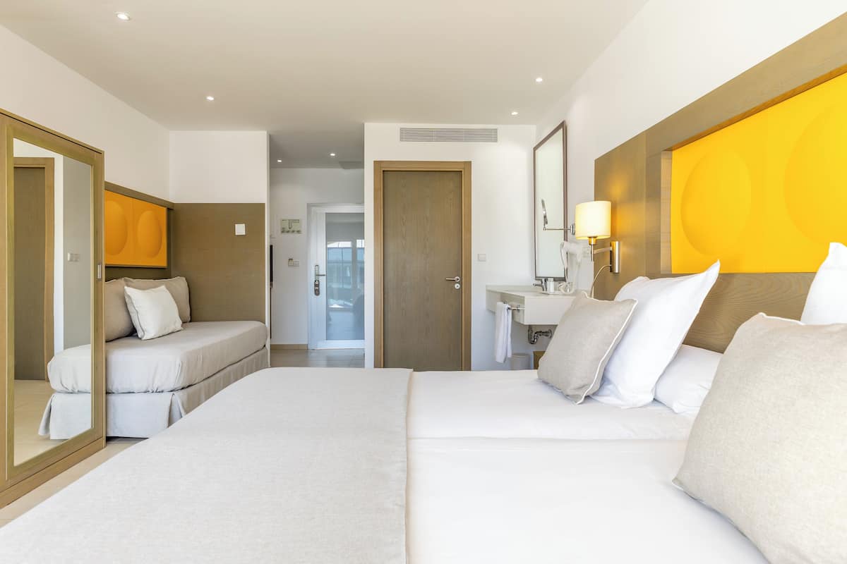 A modern hotel room with a large bed, a bedside table, a mirror, and a bright yellow accent wall.