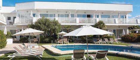 Un hotel moderno con zona de piscina, que incluye tumbonas y sombrillas.