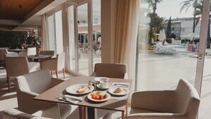 A dining area with a table set for two, a view of the pool area, and a modern interior design. - Hoposa Apartamentos Montelin (Pollenca)