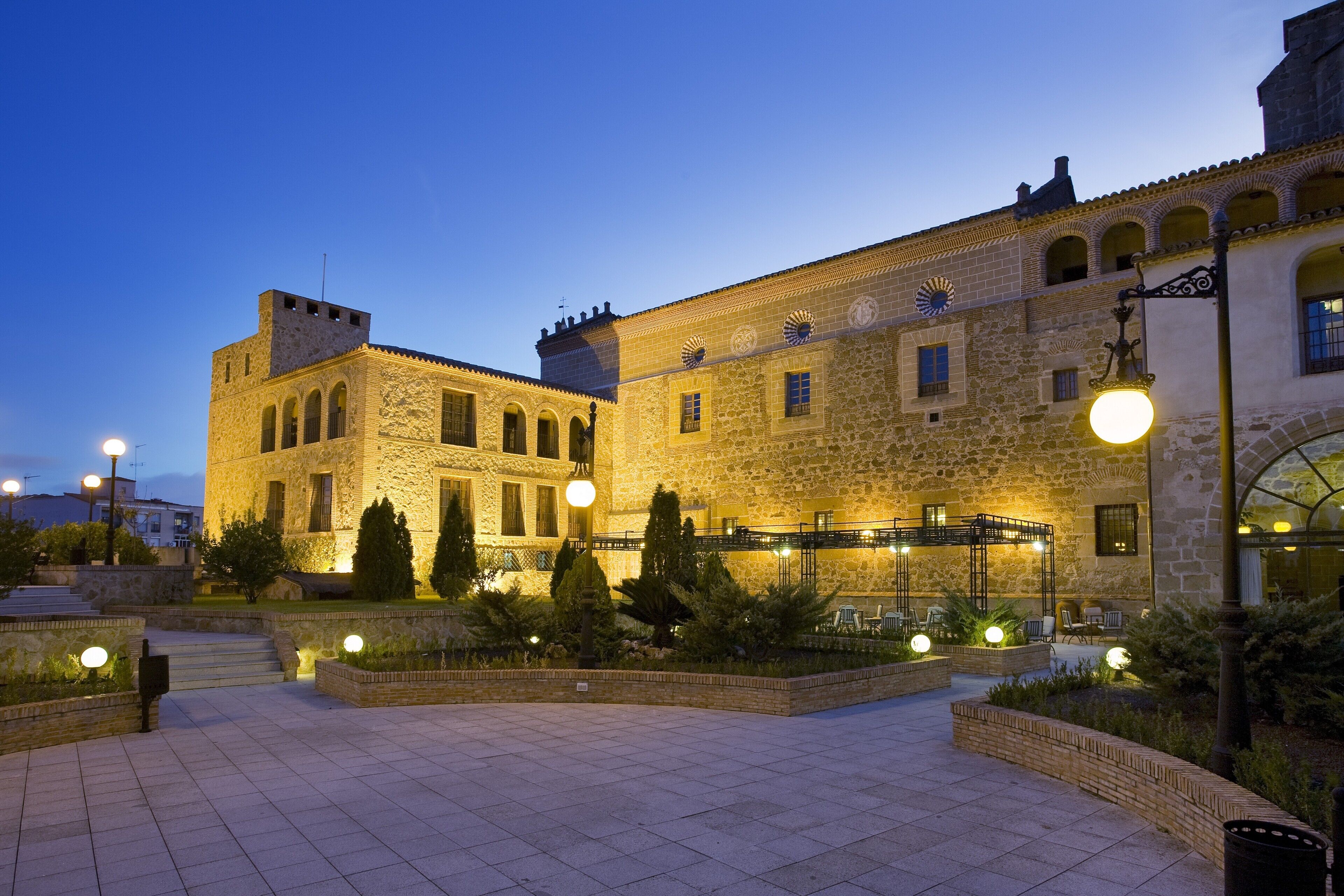 Un edificio histórico de piedra con ventanas de arco y un patio con zonas de estar y plantas.