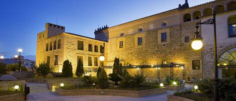 A historic stone building with arched windows and a courtyard with seating areas and plants.