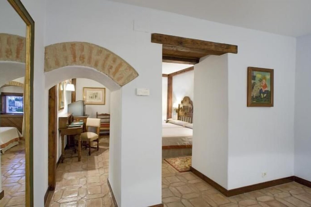 A hallway with a desk, chair, and a bed in the background.