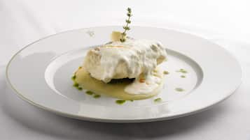 Une assiette blanche contenant un plat blanc nappé d’une sauce crémeuse et agrémenté d’une branche d’herbe aromatique.