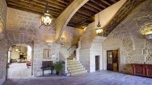 A spacious interior with stone walls, wooden beams, and a staircase leading to upper levels. - Parador de Plasencia (Plasencia)