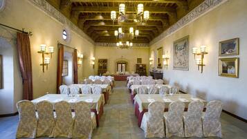 Une salle de banquet dotée de nombreuses tables rondes, chacune recouverte d’une nappe blanche et agrémentée de chaises habillées, et un lustre suspendu au plafond.