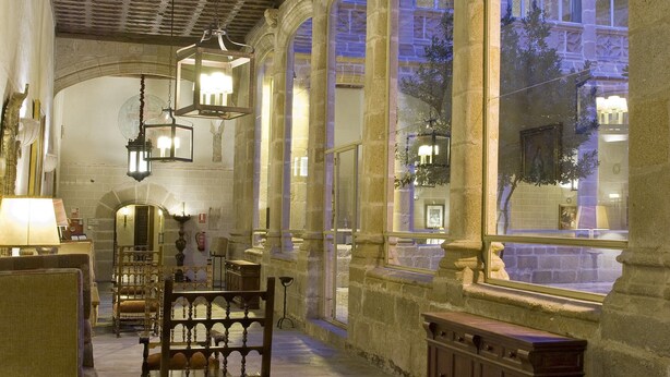 A historic interior with arched windows, stone columns, and traditional furnishings. - Parador de Plasencia (Plasencia)