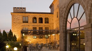 A courtyard with stone buildings, outdoor seating, and a large arched window. - Parador de Plasencia (Plasencia)