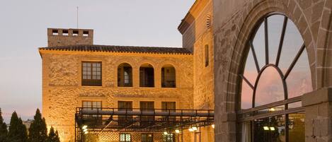 Un patio con edificios de piedra, mobiliario exterior y un amplio ventanal de arco.