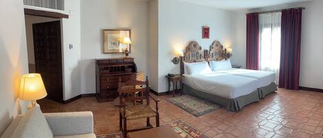 Habitación de hotel con cama, sofá, escritorio, silla, lámpara y alfombra.