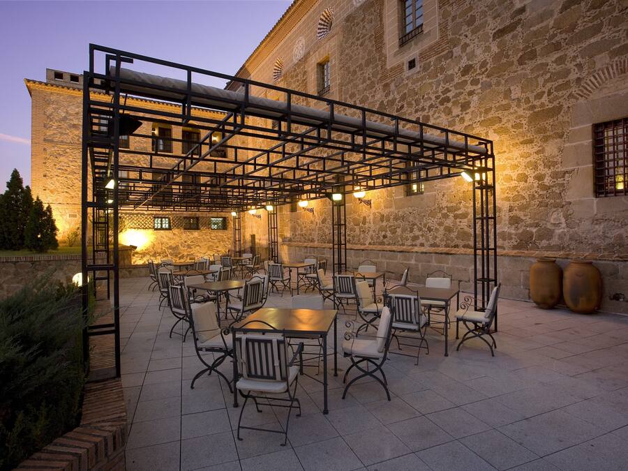 An outdoor patio area with tables and chairs, a stone building in the background, and a metal pergola structure.