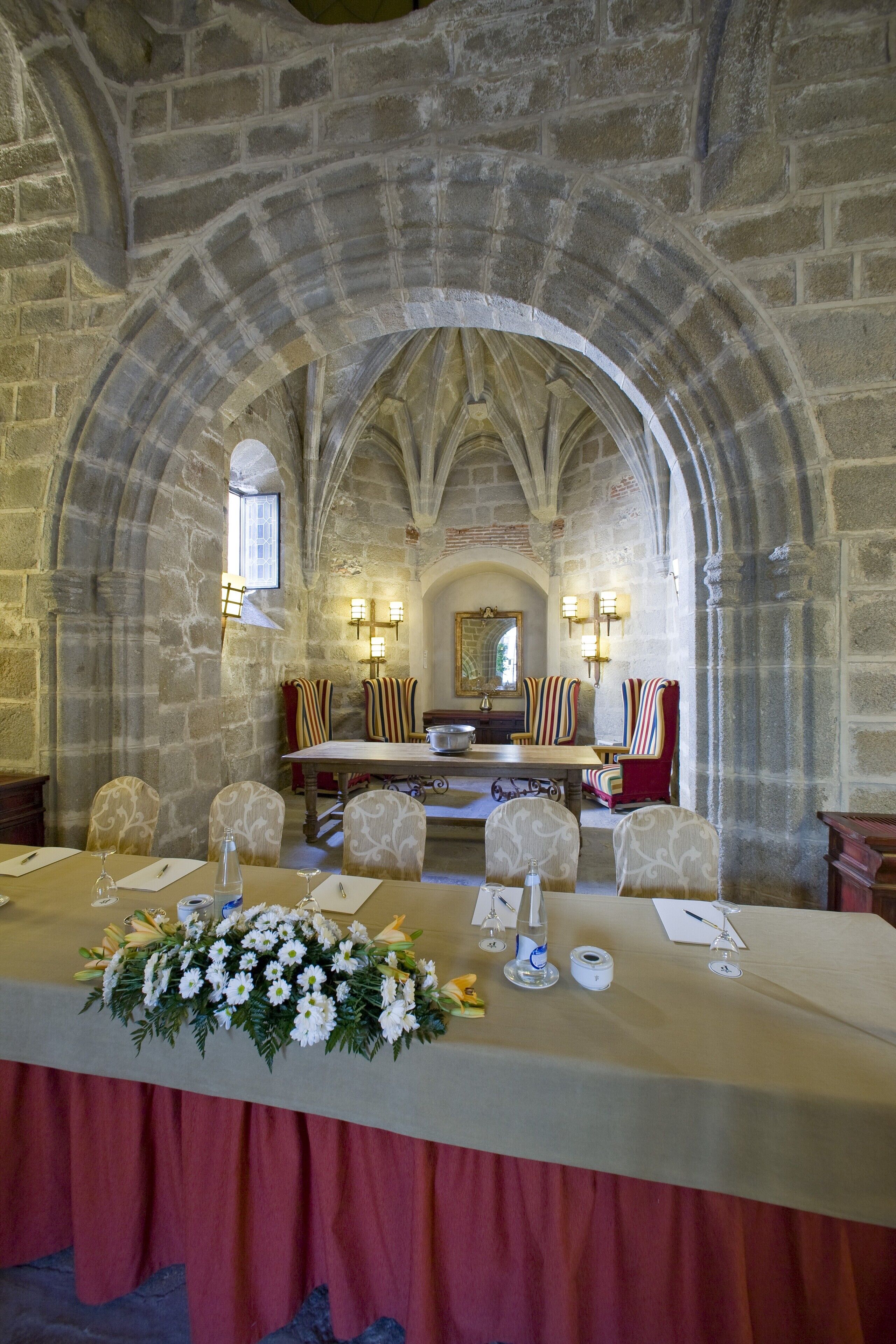 Un salón de banquetes con una larga mesa dispuesta para una comida, paredes de piedra y techos abovedados.