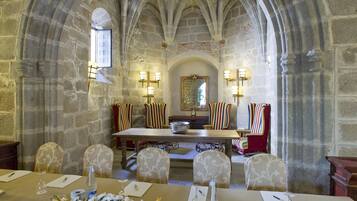 Un salón de banquetes con una larga mesa dispuesta para una comida, paredes de piedra y techos abovedados.