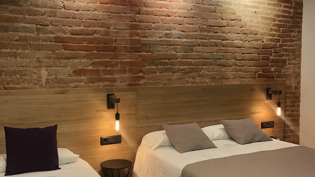 A hotel room with two beds, a brick wall, and modern lighting fixtures.