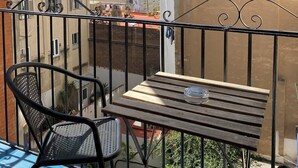 A balcony with a table and chairs, overlooking a cityscape with buildings and a clear sky.