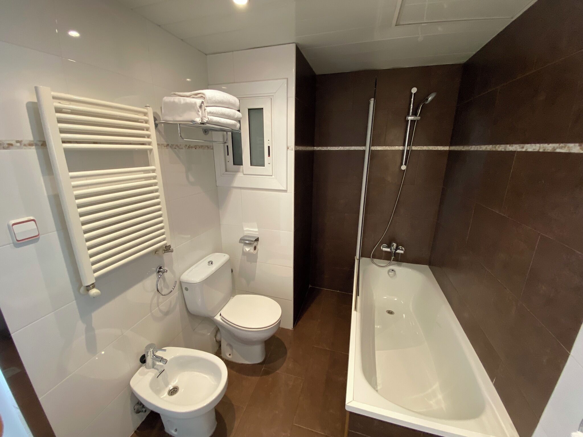 A modern bathroom with a toilet, bidet, bathtub, and towel rack.