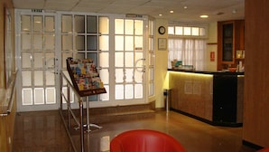 A hotel lobby with a reception desk, a bulletin board, and a clock on the wall.