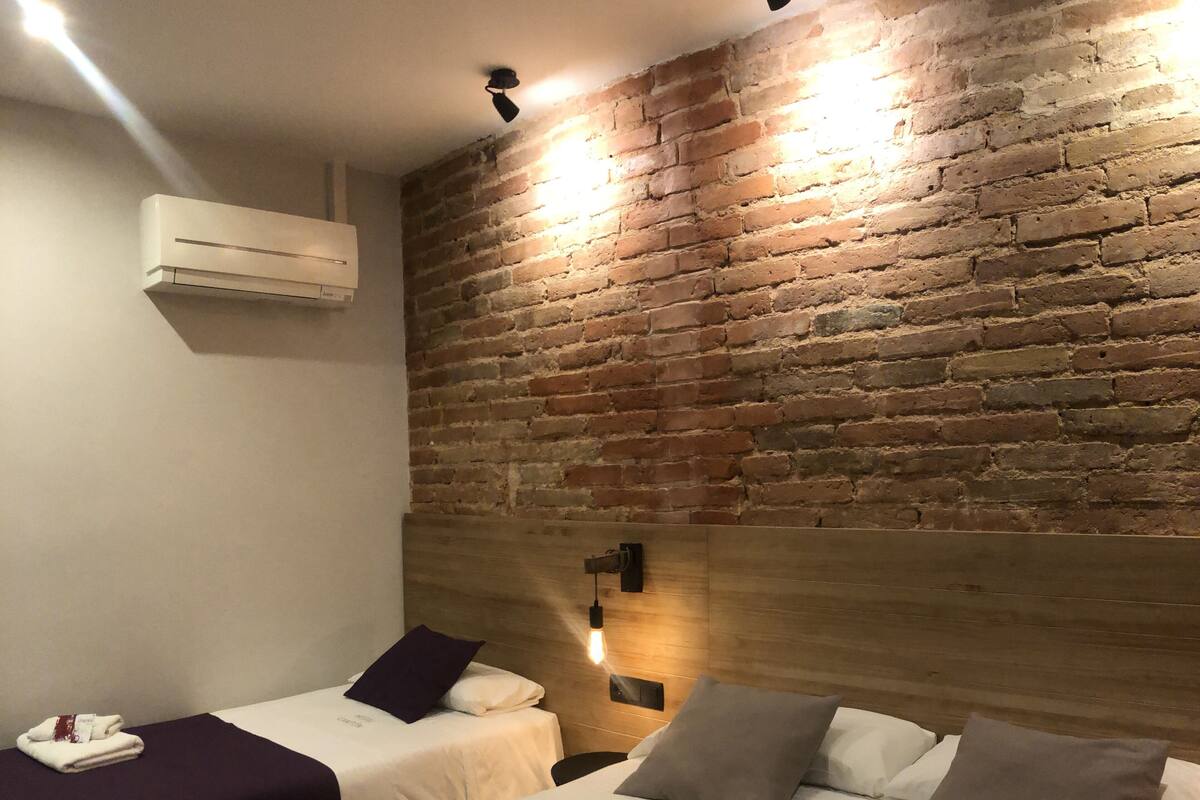A hotel room with two beds, a brick wall, and a modern light fixture.