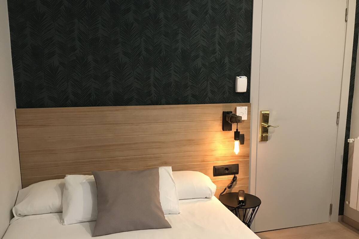 A hotel room with a wooden headboard, a bed with white and brown bedding, a bedside table with a lamp, and a wall-mounted phone.