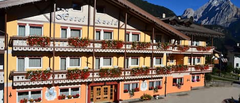 A hotel with a traditional Alpine architectural style, featuring balconies with flower boxes and a mountain backdrop.