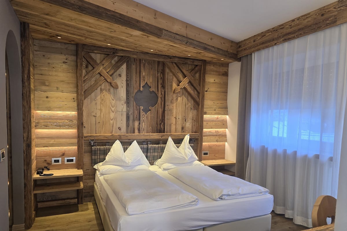 A bedroom with a wooden headboard, a bed with white linens, a bedside table, and a window with curtains.
