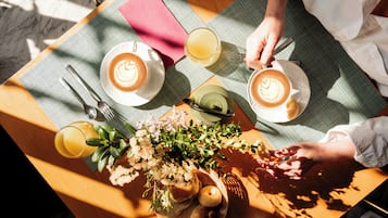 Un tavolo con due tazze di caffè, un bicchiere di succo d'arancia, un cestino di pane e una piccola pianta.